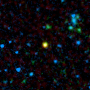 Это изображение составлено из данных инфракрасного телескопа Spitzer (синий и голубой цвет) и радиотелескопа Very Large Array (красный цвет). Желтое пятно — отдаленная галактика, в которой скрывается квазар (она видна на обоих изображениях, так как испускает и инфракрасное, и радиоизлучение). Зеленые и голубые пятна — галактики, не содержащие квазаров (фото с сайта www.spitzer.caltech.edu)