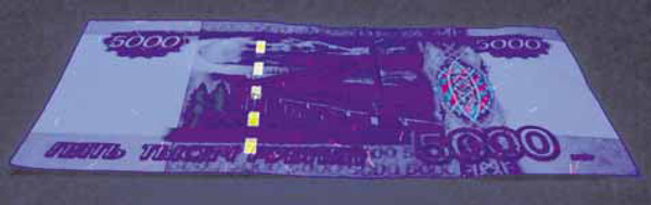 Рис. 5. Банкнота в ультрафиолетовом свете (фото автора). Прерывистая полоса слева и эмблема флуоресцируют. Изображение: «Химия и жизнь»