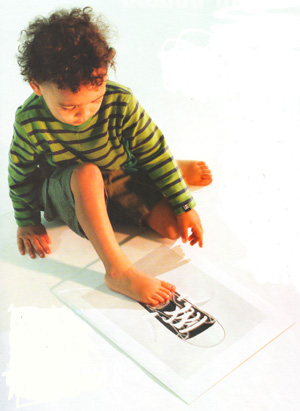 Фотографии сбивают с толку малышей, не освоивших двойственное восприятие и не осознающих, что символический объект является одновременно и самим собой (в данном случае качественной фотографией), и изображением другого предмета (кеда). Многие дети пытаются взаимодействовать с изображенными на фотографии объектами так же, как этот мальчик, старающийся всунуть ногу в кед (фото: «В мире науки»)