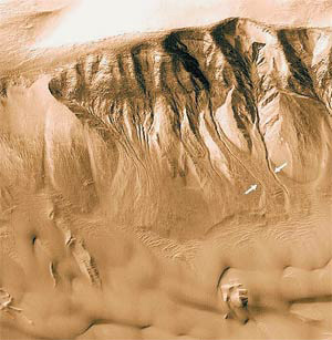 Рис. 10. Осыпи грунта и нитевидные овраги (показаны стрелками) на склоне кратера (42,4°S, 158,2°W). Овраги похожи на следы земных горных рек, но, в отличие от земных оврагов, они не расширяются, а сужаются вниз по склону. (MGS MOC Release No. MOC2-320. NASA/JPL/MSSS.) Изображение: «Наука и жизнь»